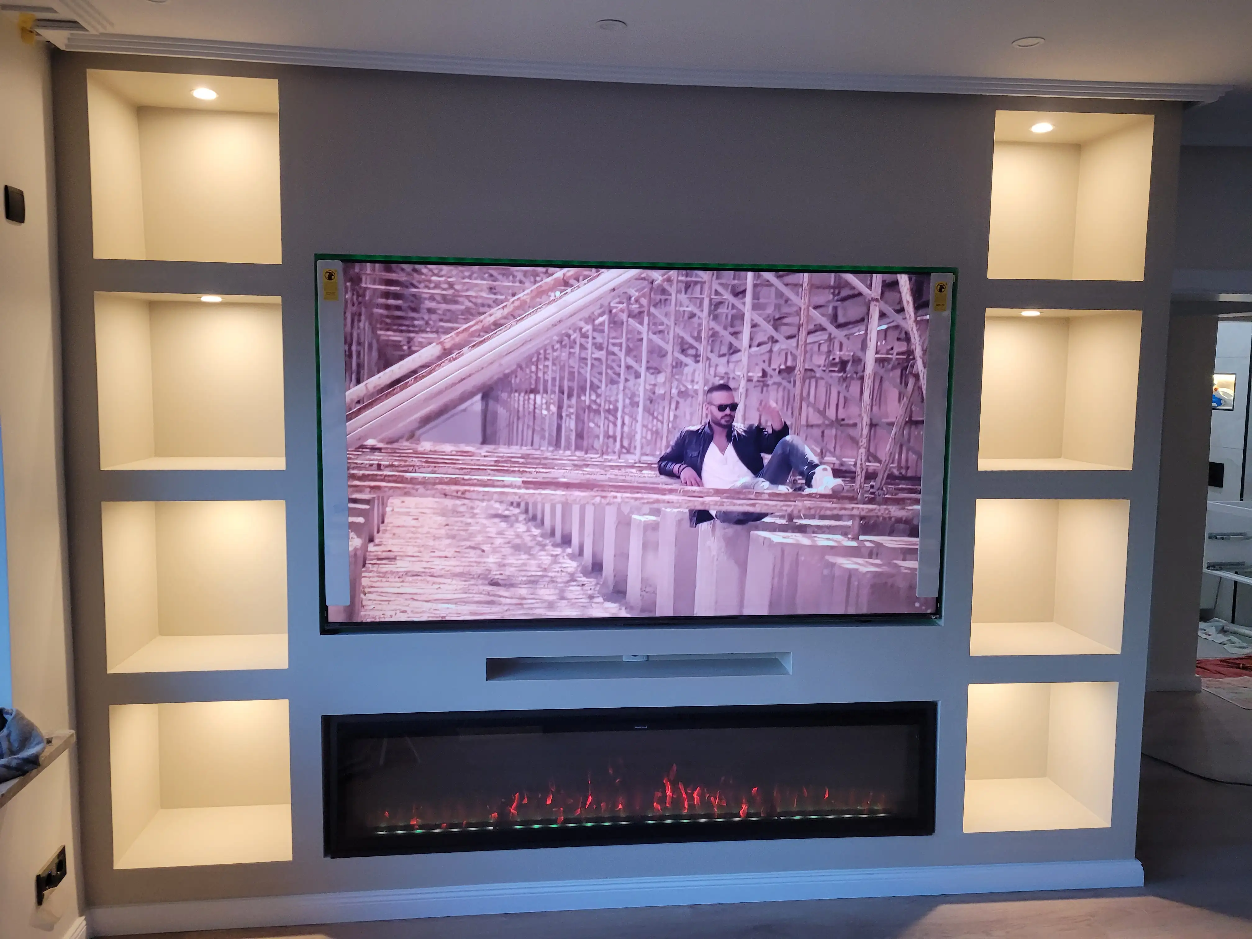 Fernsehrwand mit in der Wand eingebauten Regalen rechts und links und ein Feuer-Display unten mit Steckdosen, wobei das Fernsehr mittig angehängt ist