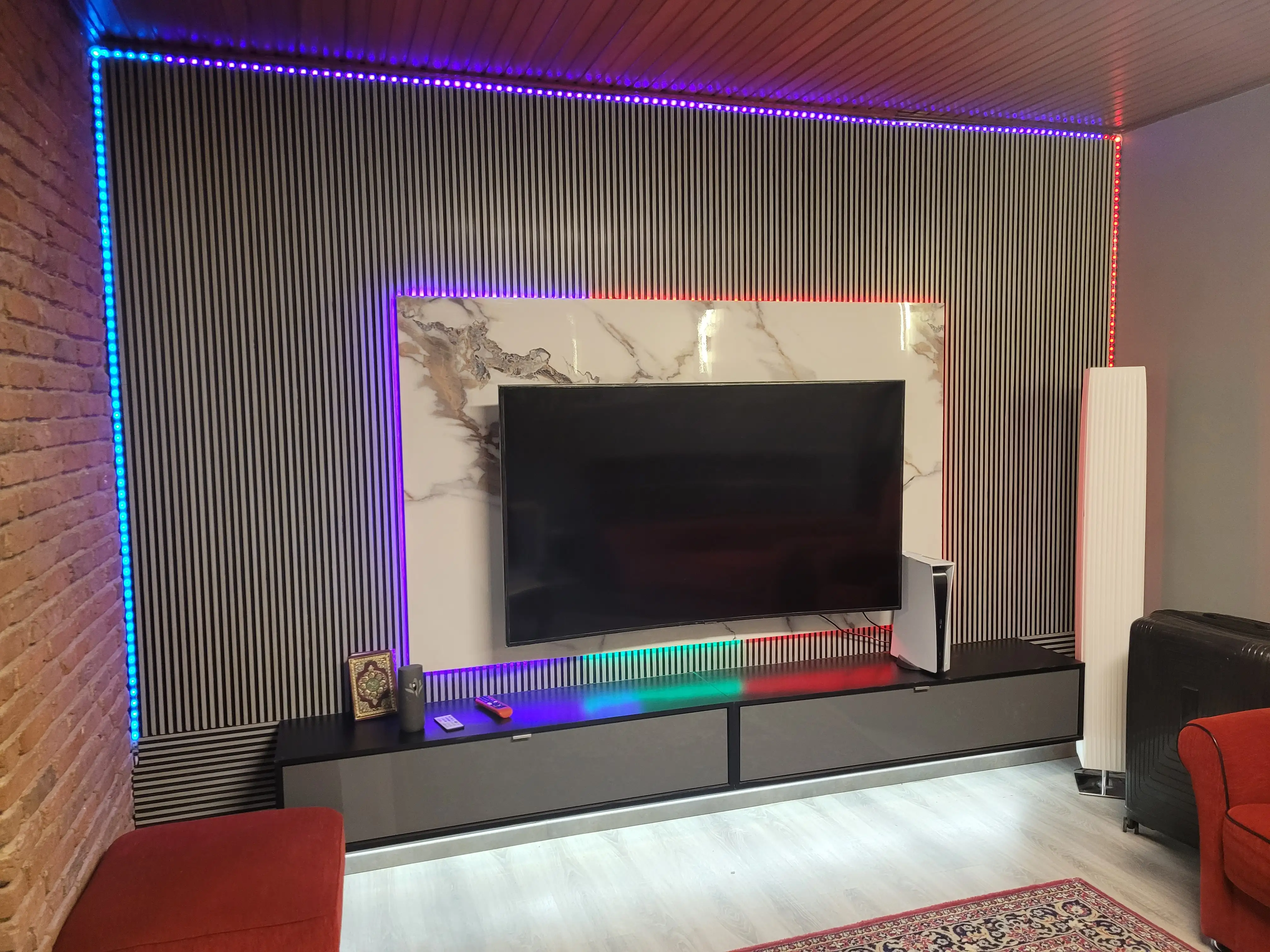 Ein Wohnzimmer mit Holzpaneelen-Wand und eine zentrierten Marmorplatte, worauf ein Fernsehr montiert ist mit versteckten LED.
