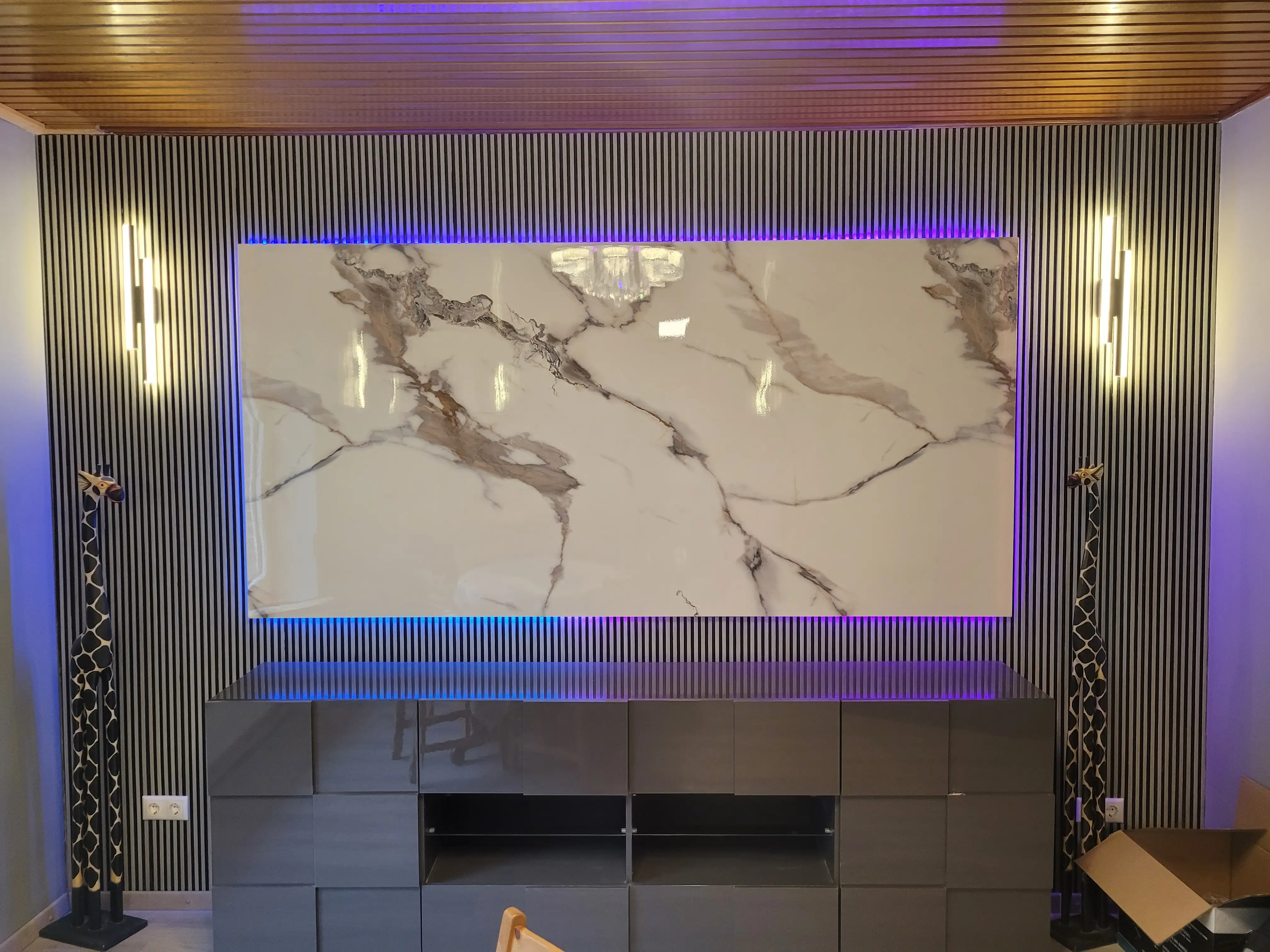 Stylische TV-Wand mit großer Marmoroptik-Platte, LED-Hinterbeleuchtung und modernen Lamellen an der Wand.